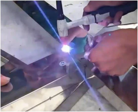 A close-up photograph of a manual welder performing traditional TIG or argon arc welding on a stainless steel pipe, creating a prominent weld bead.